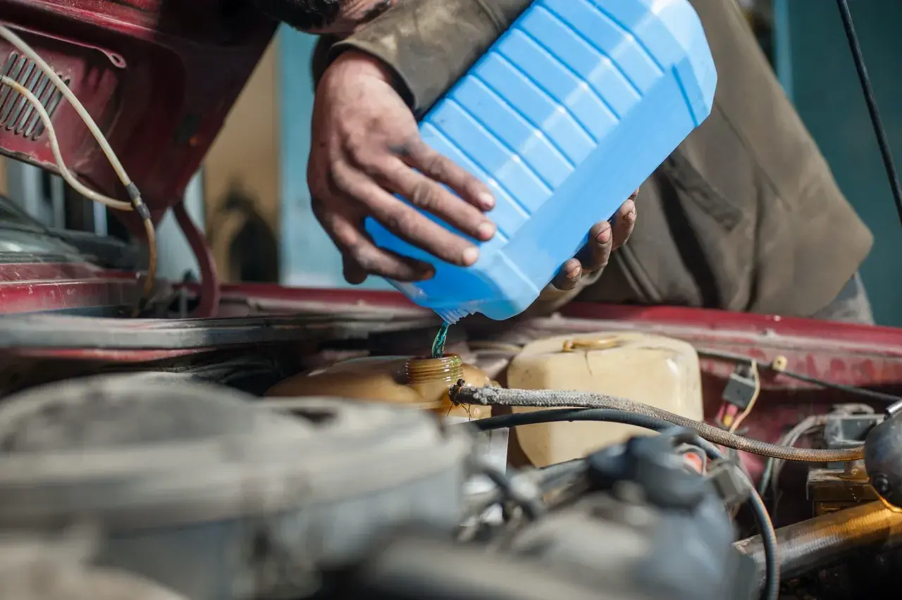 Mecánico vierte líquido refrigerante azul para limpiar radiador coche.