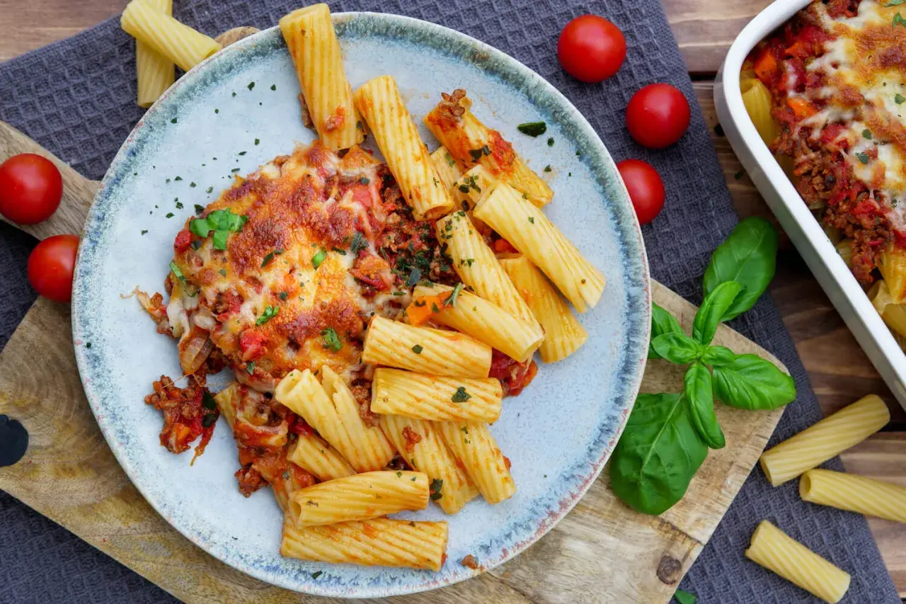 Herzhaftes Bolognese Gratin mit Rigatoni, überbacken mit geschmolzenem Käse, garniert mit frischem Basilikum und Tomaten.