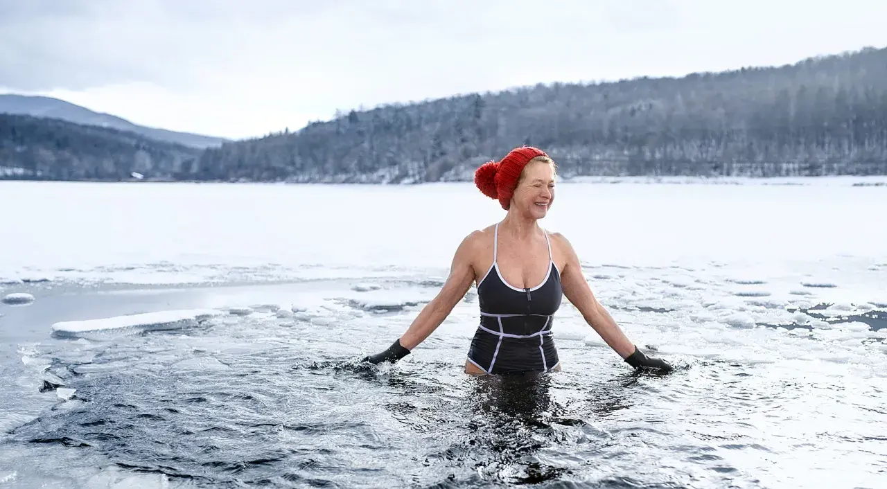 Frau genießt eisbaden in gefrorenem See. Sie lacht und fragt sich, ob eisbaden gesund ist.