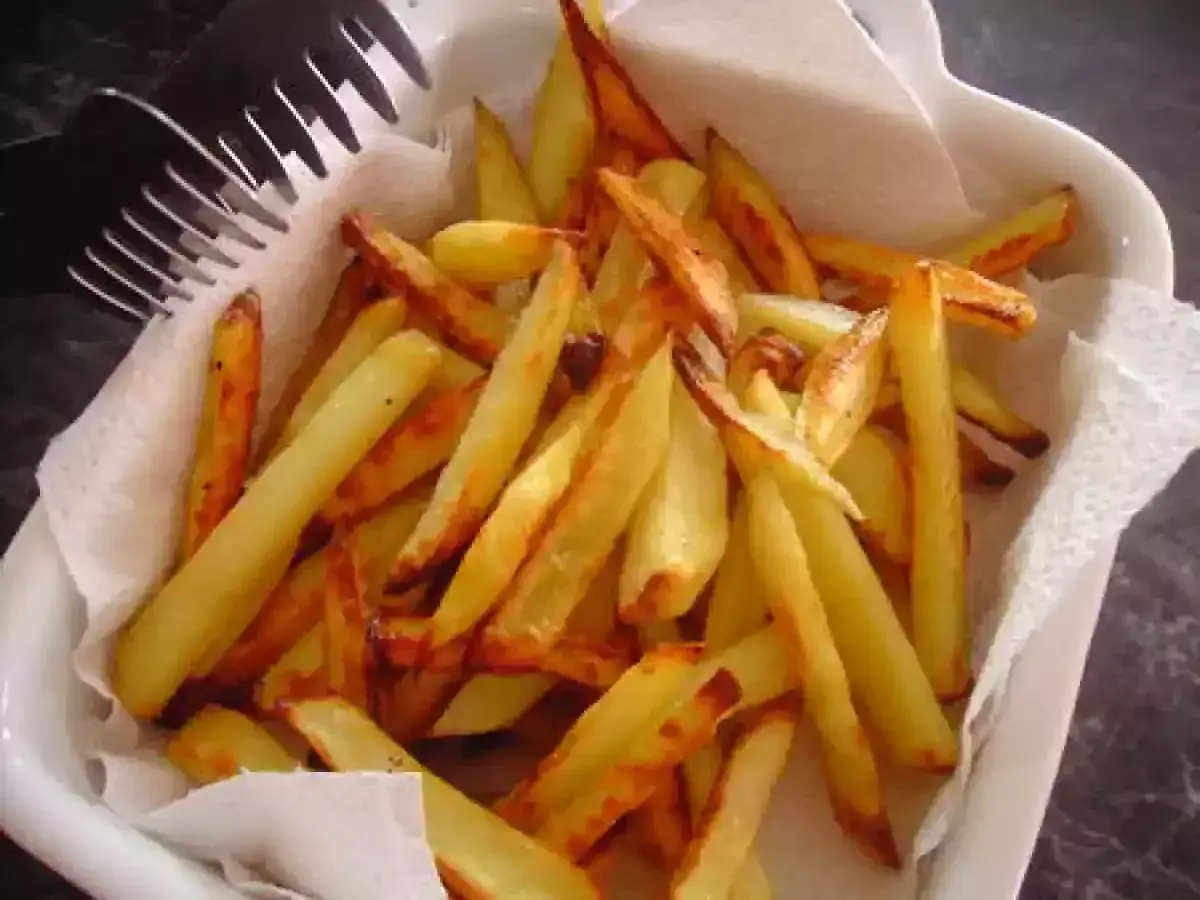 Un plat blanc rempli de délicieuses frites au four, dorées et croustillantes, prêtes à être dégustées. Une fourchette est posée sur le bord.