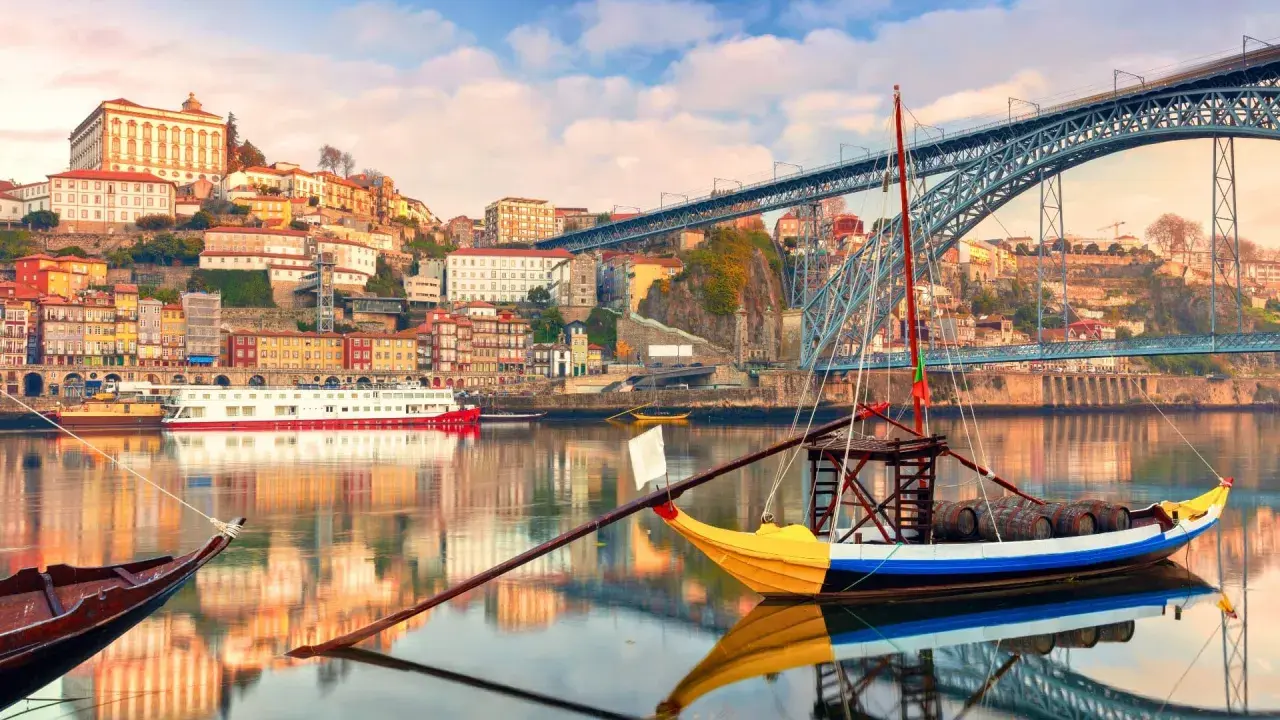 Barcos tradicionales navegan por el río Duero, con la colorida Ribeira y el puente Dom Luís I al fondo. Perfectas rutas cerca de Oporto para explorar.