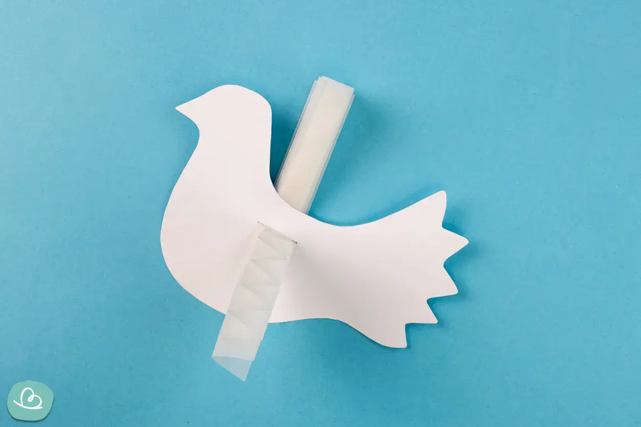 Eine weiße Papier-Friedenstaube wird mit Klebeband befestigt. Bastelanleitung für eine Friedenstaube.