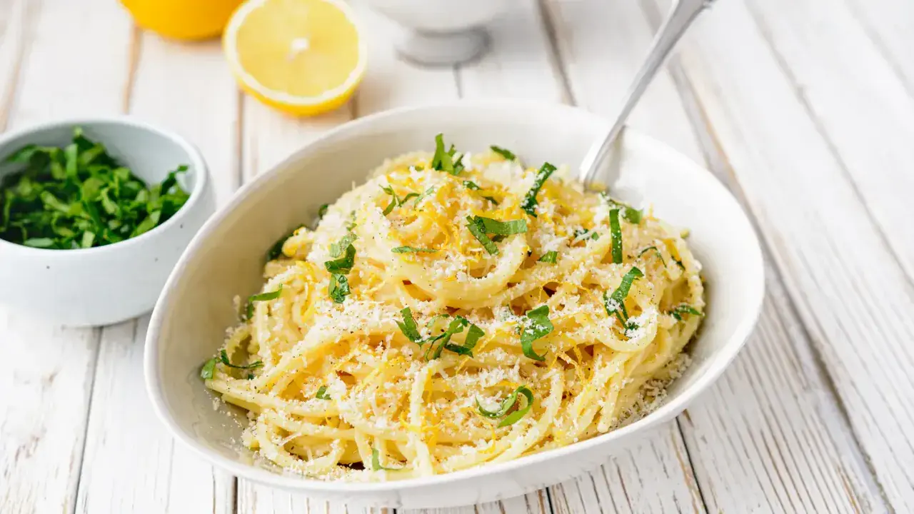 Un plat de pâtes au citron, garni de persil frais et de parmesan râpé, prêt à être dégusté.