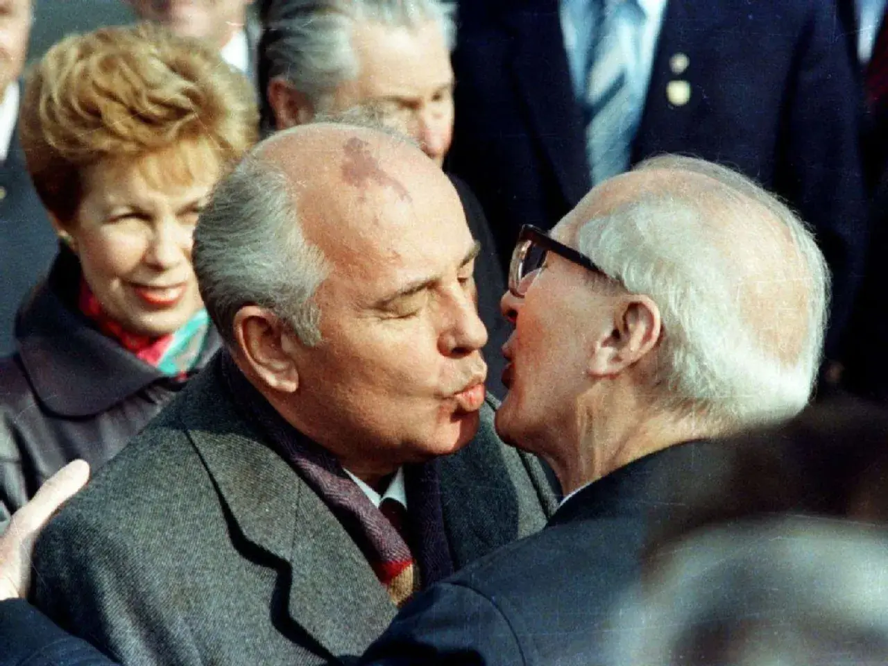 Gorbatschow und Honecker im Bruderkuss. Eine Frau im Hintergrund lächelt.