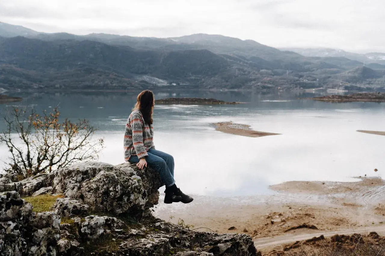 Frau sitzt auf Felsen mit Blick auf einen See und Berge. Ein perfekter Moment während eines Montenegro Roadtrips.