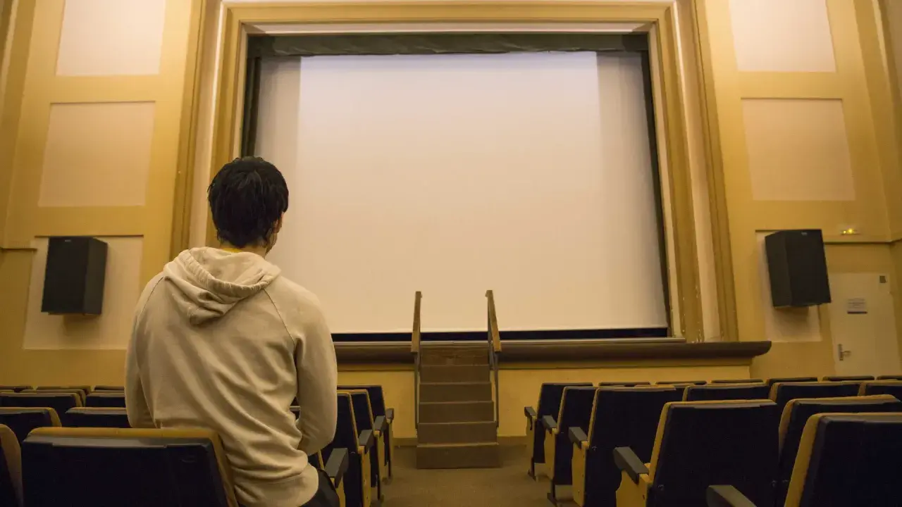 Un joven espera en un cine vacío, listo para disfrutar de una película.