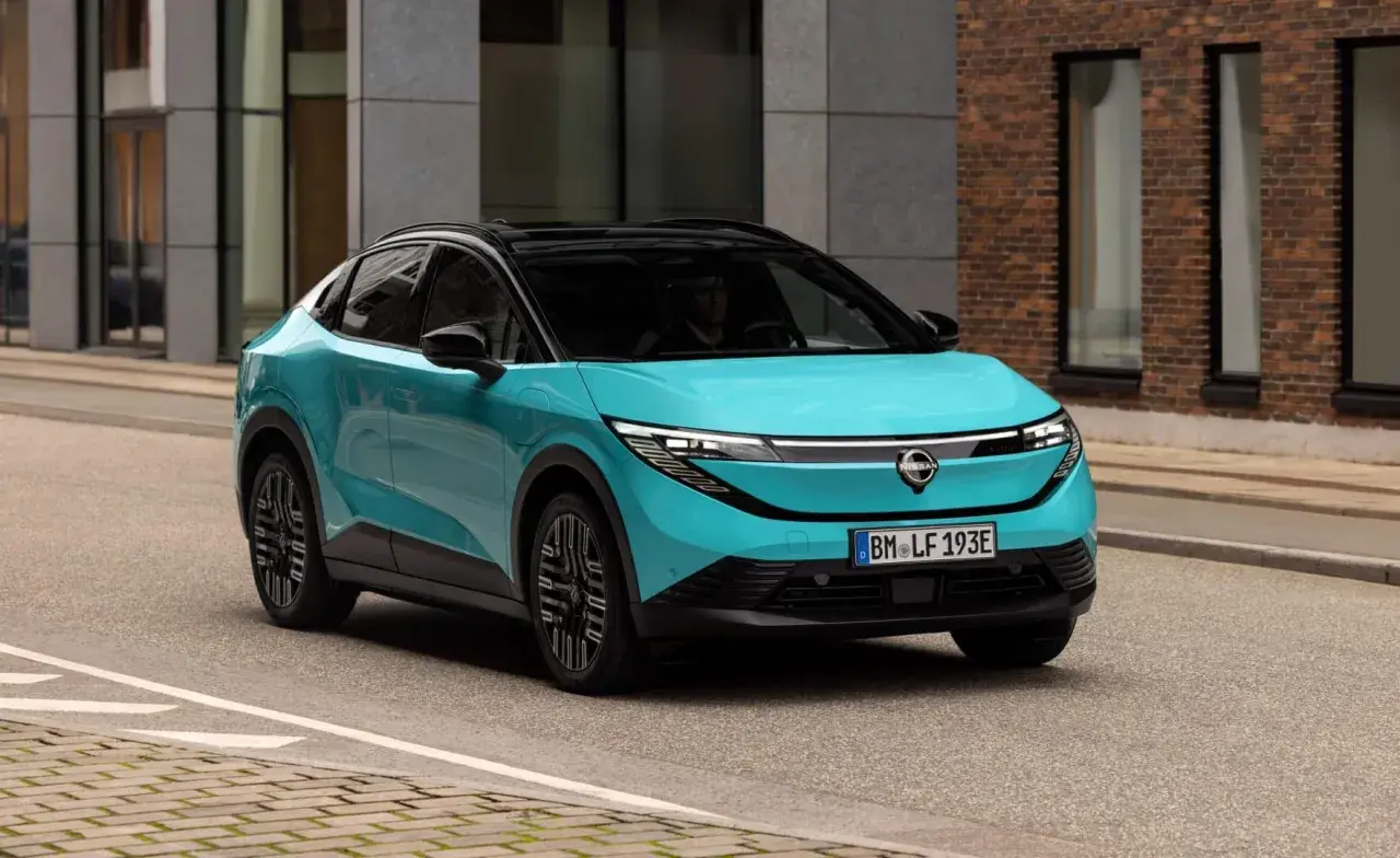 La Nissan Leaf 2026, in un vivace color acquamarina, sfreccia su una strada urbana, con un design futuristico che cattura l'attenzione.