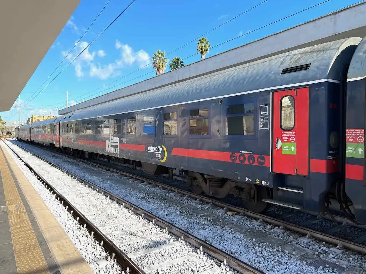 Ein langer Zug mit der Aufschrift "Intercity notte" und "DELUXE" steht am Bahnsteig. Vielleicht geht es **mit dem Zug nach Griechenland**?