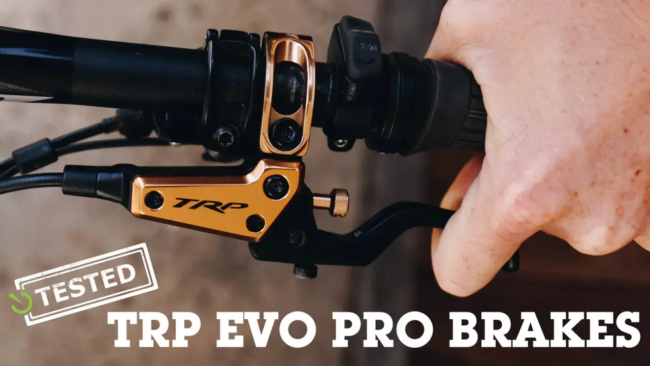 A hand squeezes a black brake lever on a bicycle handlebar. The gold TRP EVO PRO BRAKES are featured in this review.