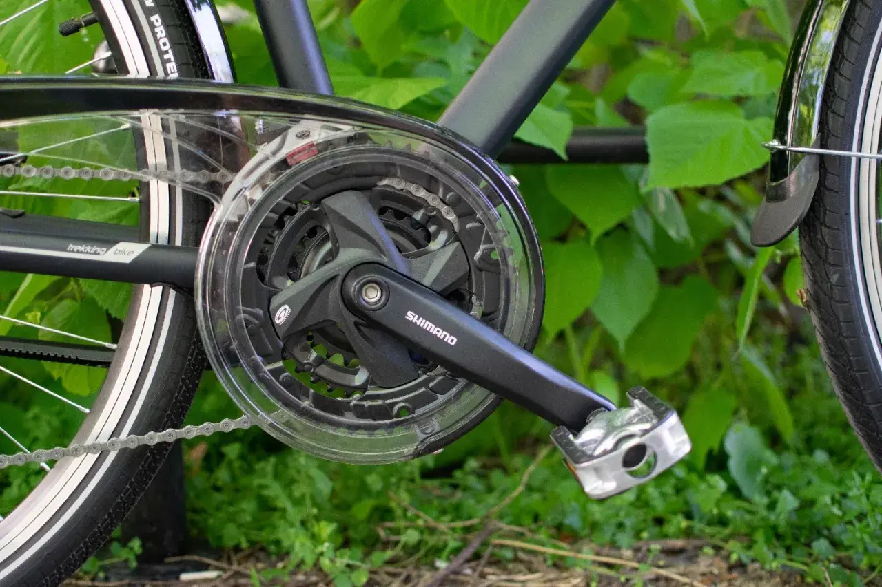 Część napędu roweru trekkingowego Shimano z korbą i zębatkami. Gotowy do jazdy po zielonym tle.