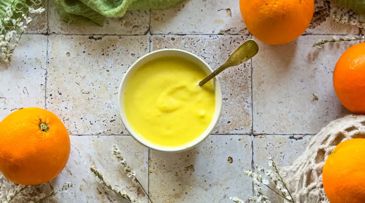 Crema gialla e liscia in una ciotola, con arance fresche intorno. Un cucchiaio dorato è immerso nella crema, che ricorda il sapore del sale all'arancia.