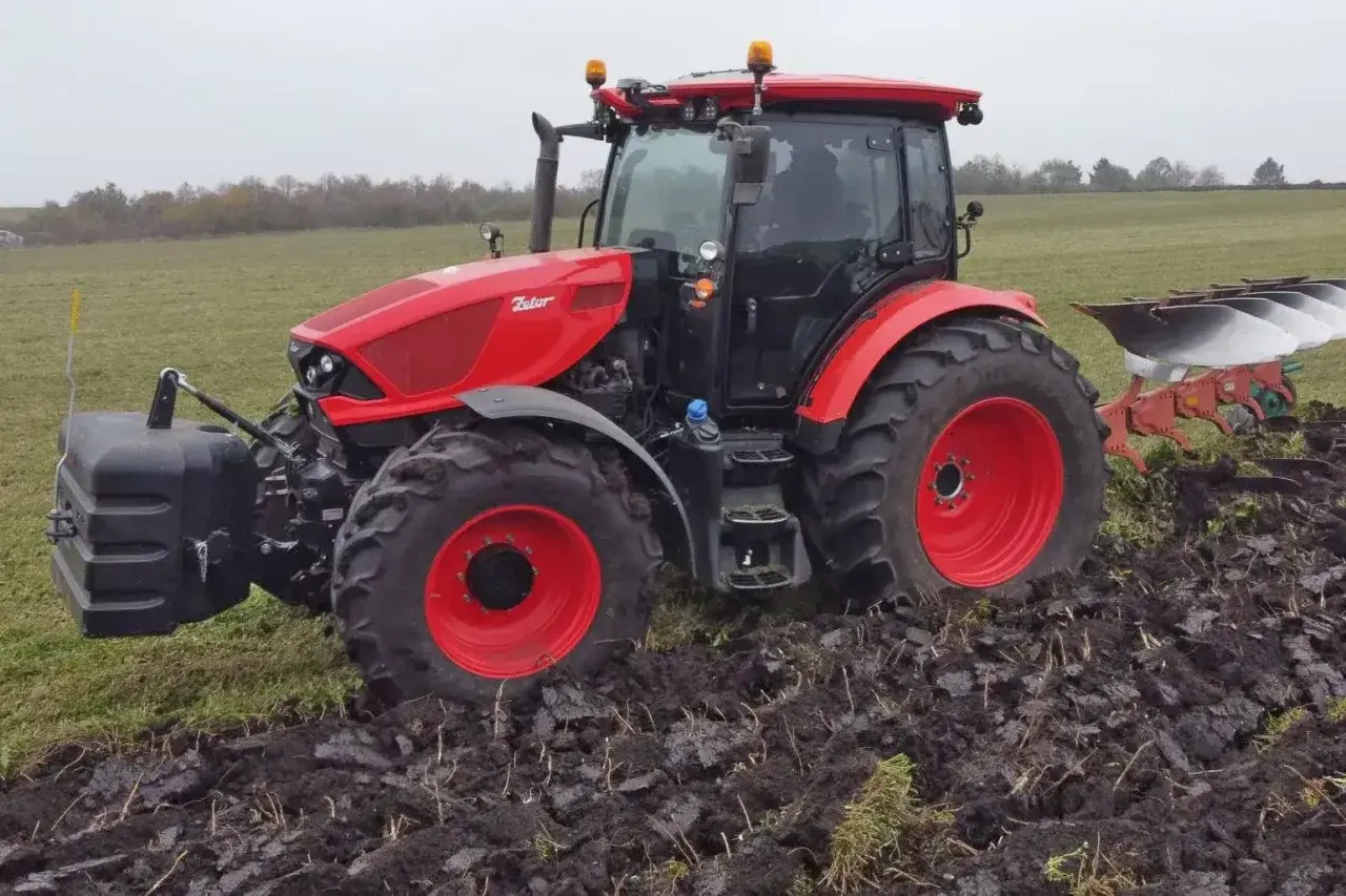 Czerwony ciągnik Zetor 6245 z pługiem orze pole w pochmurny dzień.