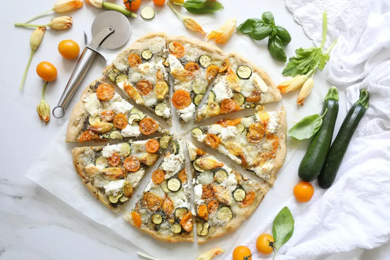 Gesunder pizzateig mit Zucchini, Kirschtomaten und Mozzarella, garniert mit Basilikum und Zucchiniblüten.