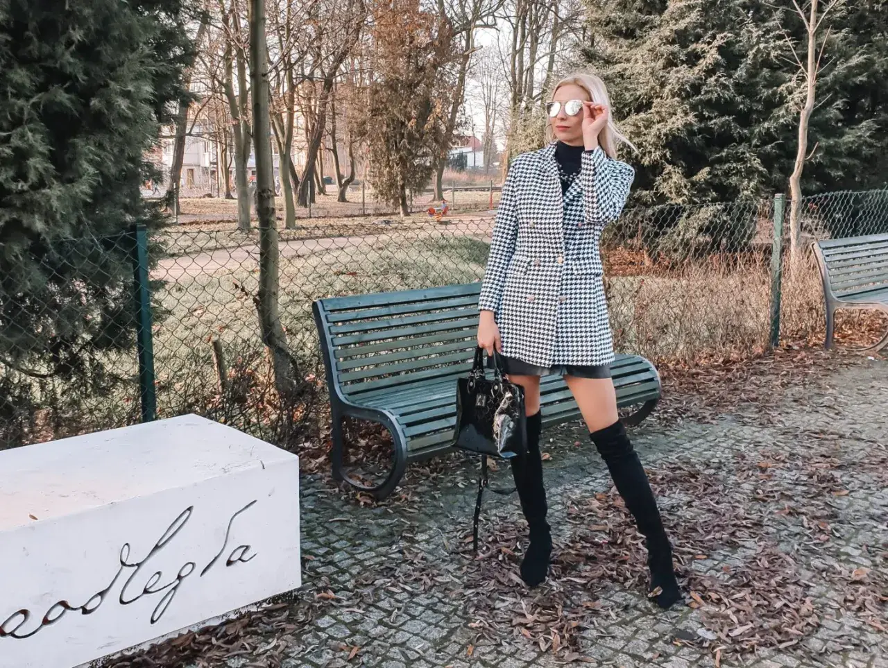 Elegancka sukienka w pepitkę, idealna na jesienne stylizacje. Kobieta w okularach przeciwsłonecznych i kozakach prezentuje modny zestaw.
