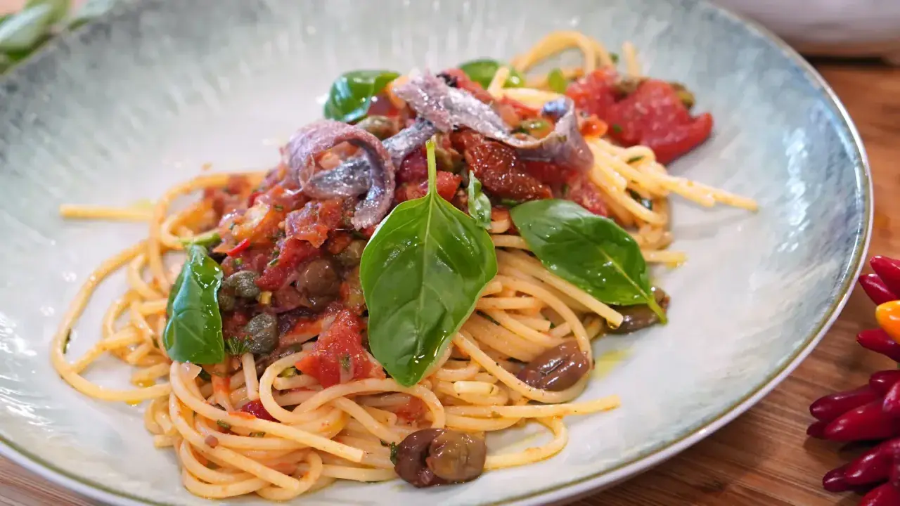 Spaghetti Puttanesca mit Sardellen, Oliven, Kapern und frischem Basilikum auf einem Teller.