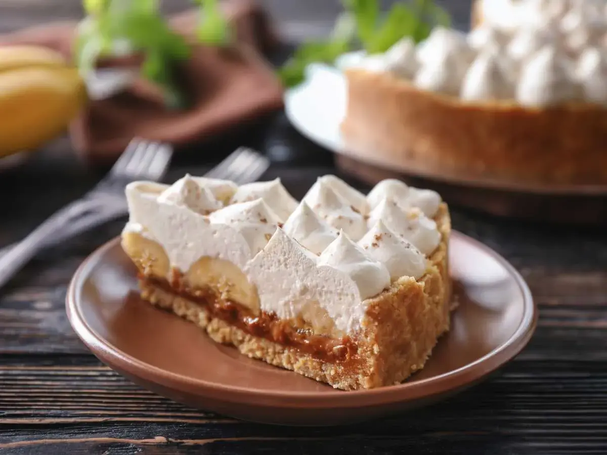 Rebanada de tarta banoffee con plátano, dulce de leche y crema batida, espolvoreada con canela.