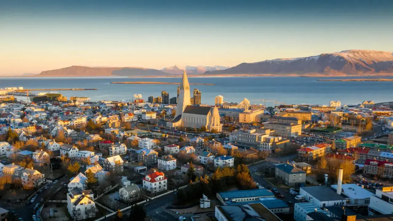 Fakta om Island: Reykjaviks ikoniska kyrka Hallgrímskirkja reser sig över staden med havet och snöklädda berg i bakgrunden.