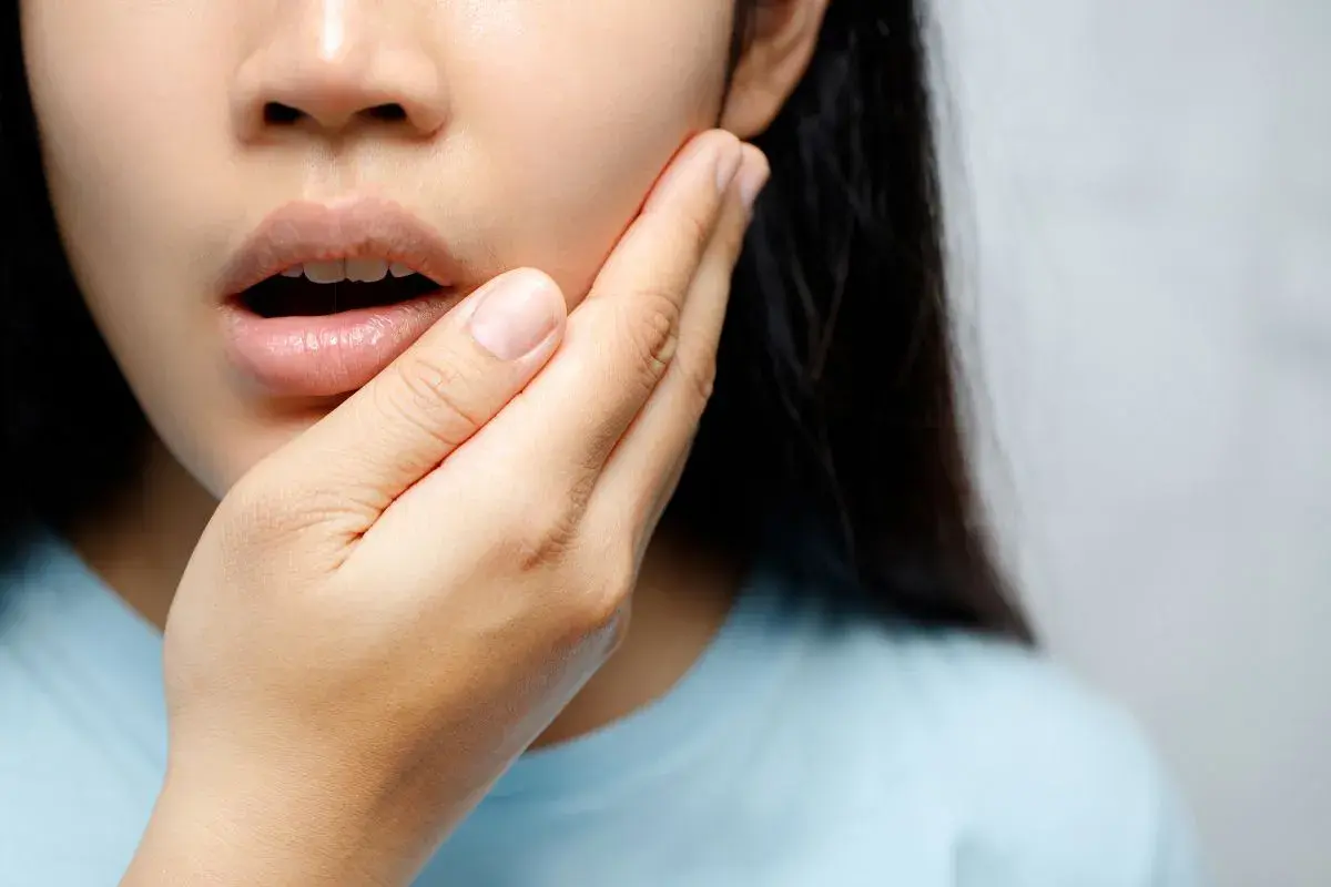 Mujer con mano en la mejilla, experimentando dolor de dientes al quitar Invisalign.