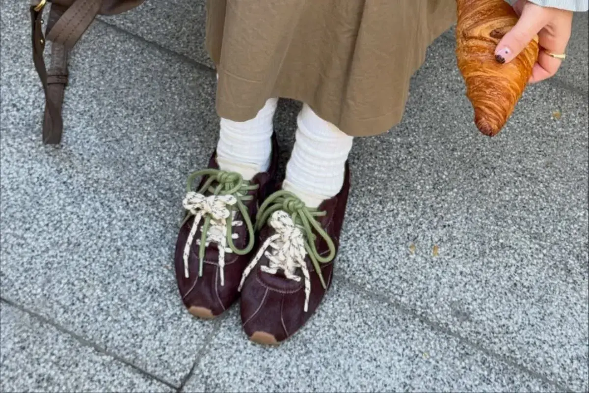 Modne sneakersy 2026 w bordowym kolorze, z zielonymi i białymi sznurówkami, idealne na spacer z croissantem.