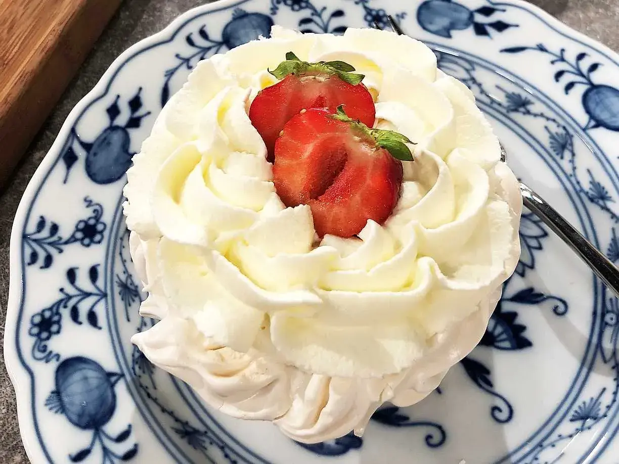 En liten pavlova med fluffig grädde och färska jordgubbar på en vacker blåvit tallrik. En perfekt liten dessert!