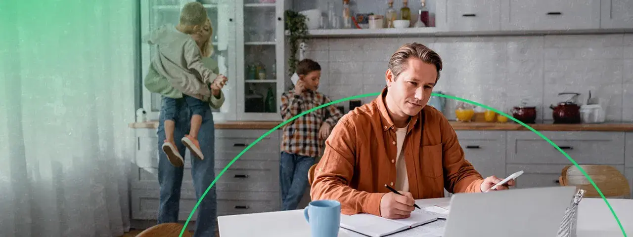 Mężczyzna w pomarańczowej koszuli pracuje przy laptopie, podczas gdy rodzina jest w tle.