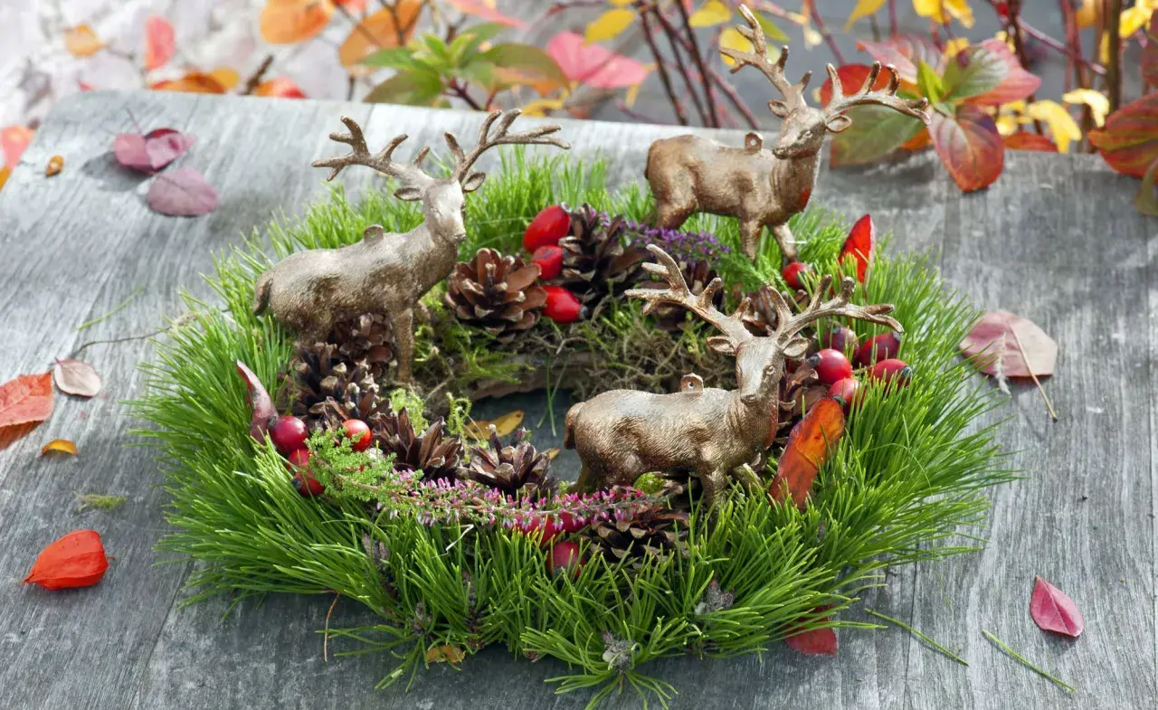 Drei Hirschfiguren schmücken einen grünen Kranz mit Tannenzweigen, Zapfen und roten Beeren. Tolle Herbstkranz Ideen für Ihr Zuhause.