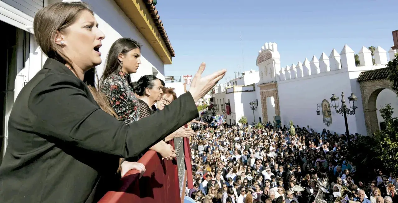Mujeres en un balcón observan una multitud y escuchan saetas populares.