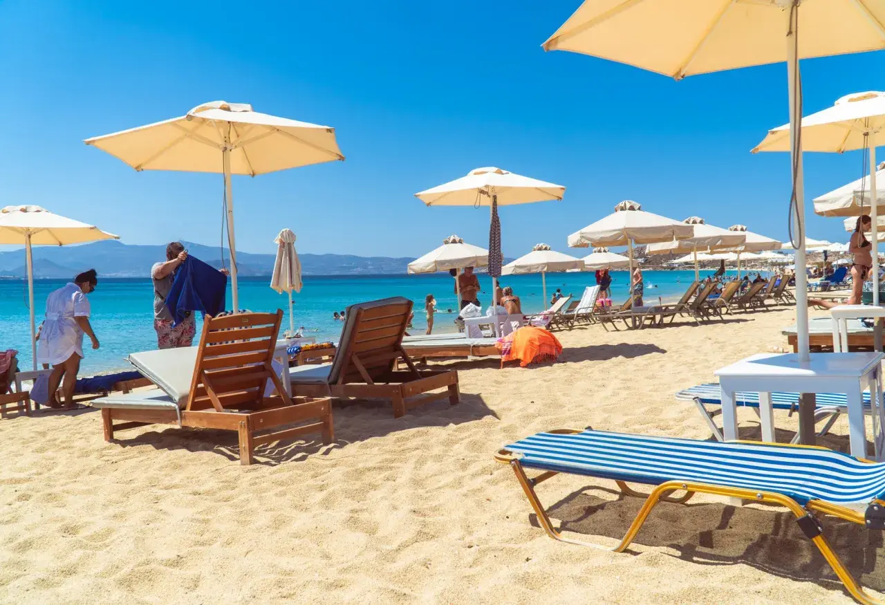 Słoneczny dzień na plaży Naxos. Leżaki pod parasolami, turkusowa woda i góry w tle.