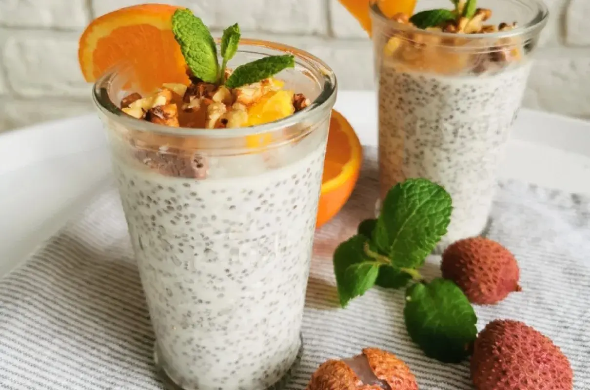 Pudding chia z pomarańczą i orzechami, ozdobiony miętą i owocami lychee.
