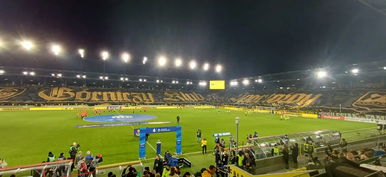Piłkarze GKS Katowice i Górnika Zabrze na murawie. Na trybunach ogromna oprawa z napisem "Górniczy Klub".