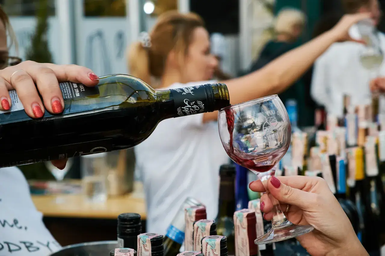 Rödvin hälls upp i ett glas, perfekt vin till lutfisk. Bakgrunden visar en festlig sammankomst med fler vinflaskor.