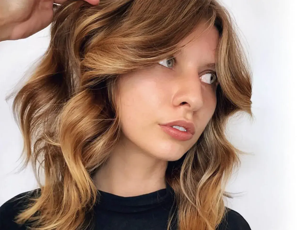 Mujer con cabello castaña iluminada, con ondas suaves y reflejos dorados que resaltan su rostro.