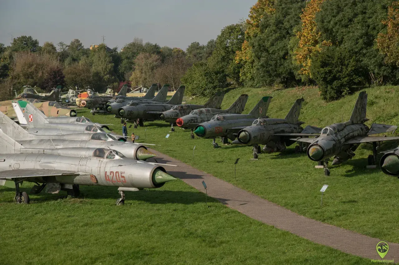 Samoloty wojskowe na trawie w Muzeum Lotnictwa w Krakowie. Widać myśliwce MiG-21 i inne maszyny.