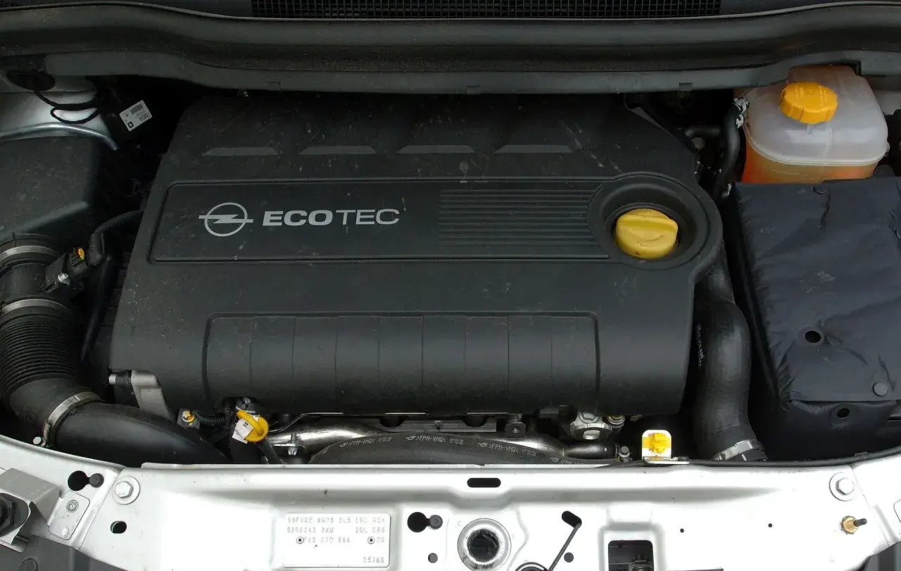 Silnik Ecotec w Oplu Zafira B. Widoczny czarny plastikowy dekiel z logo Opla i napisem Ecotec, żółty korek oleju i zbiorniczek płynu chłodniczego.