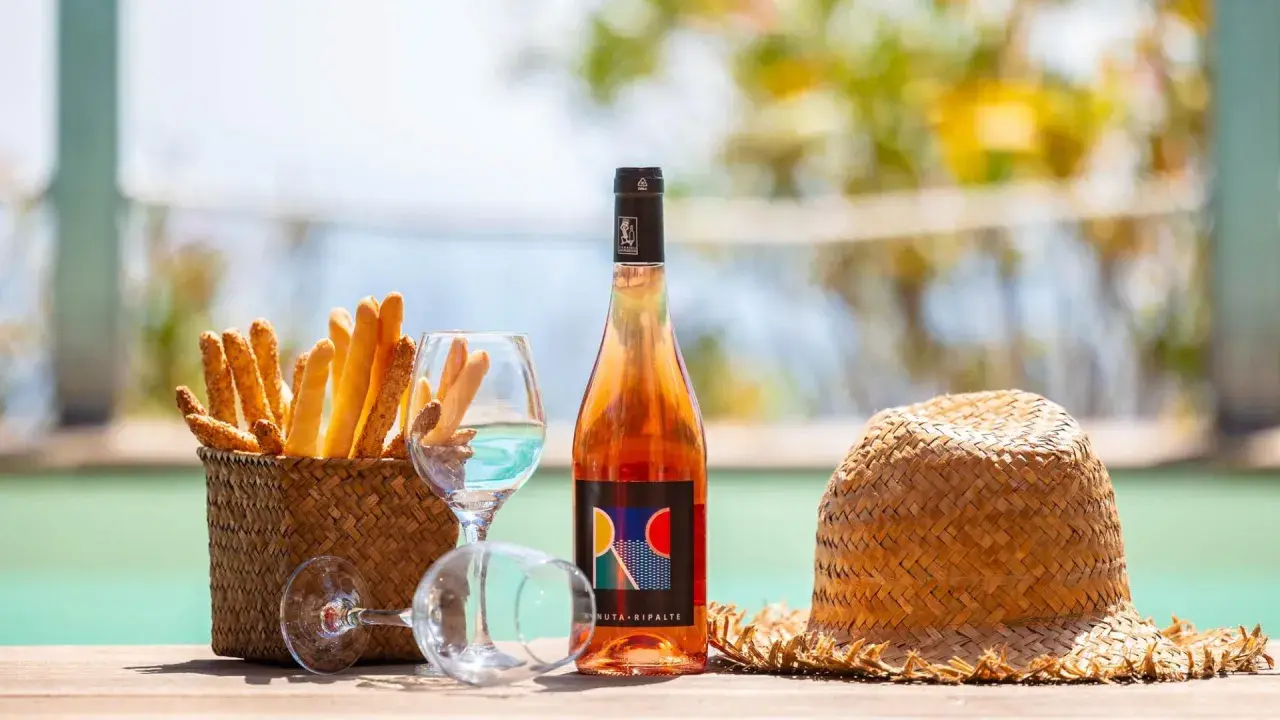 Un bicchiere di vino dolce dell'Elba, grissini croccanti e un cappello di paglia, perfetti per un aperitivo al mare.