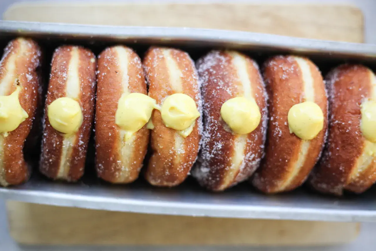 Una fila di bomboloni alla crema, cosparsi di zucchero, pronti per essere gustati.