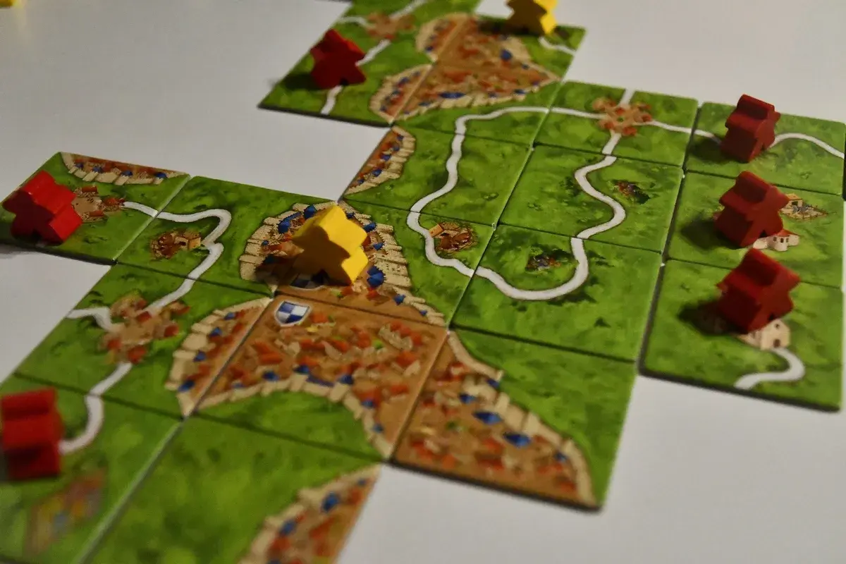 Rozgrywka w Carcassonne: czerwoni i żółci rycerze zajmują pola z miastami i drogami, budując średniowieczny krajobraz.