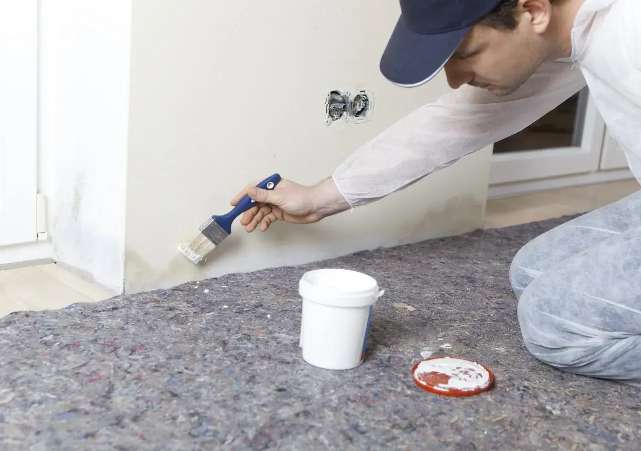 Maler streicht mit Pinsel über Wasserflecken an der Wand, um sie zu überdecken.