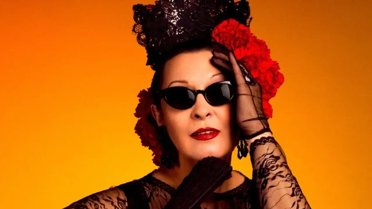 Jarcha, con su estilo inconfundible, evoca un martirio flamenco con encaje negro, gafas oscuras y flores rojas sobre fondo naranja.