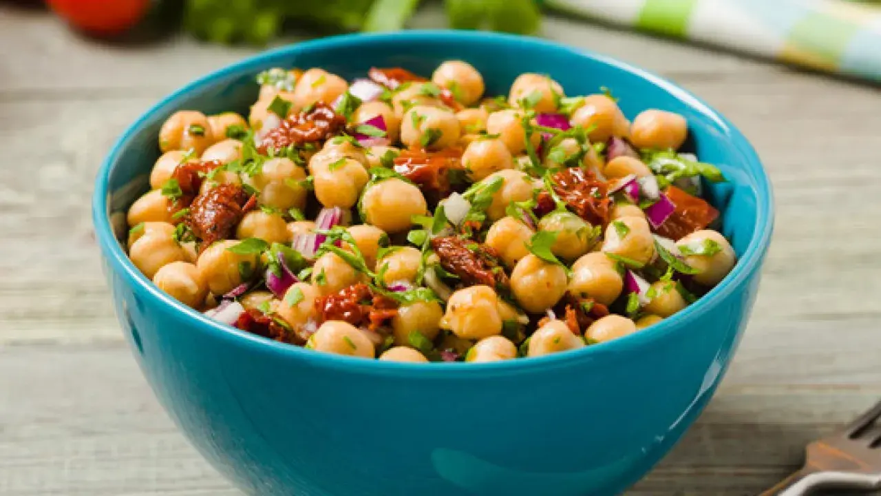 Ensalada de garbanzos fresca y colorida con tomate seco y cebolla morada en un cuenco azul.