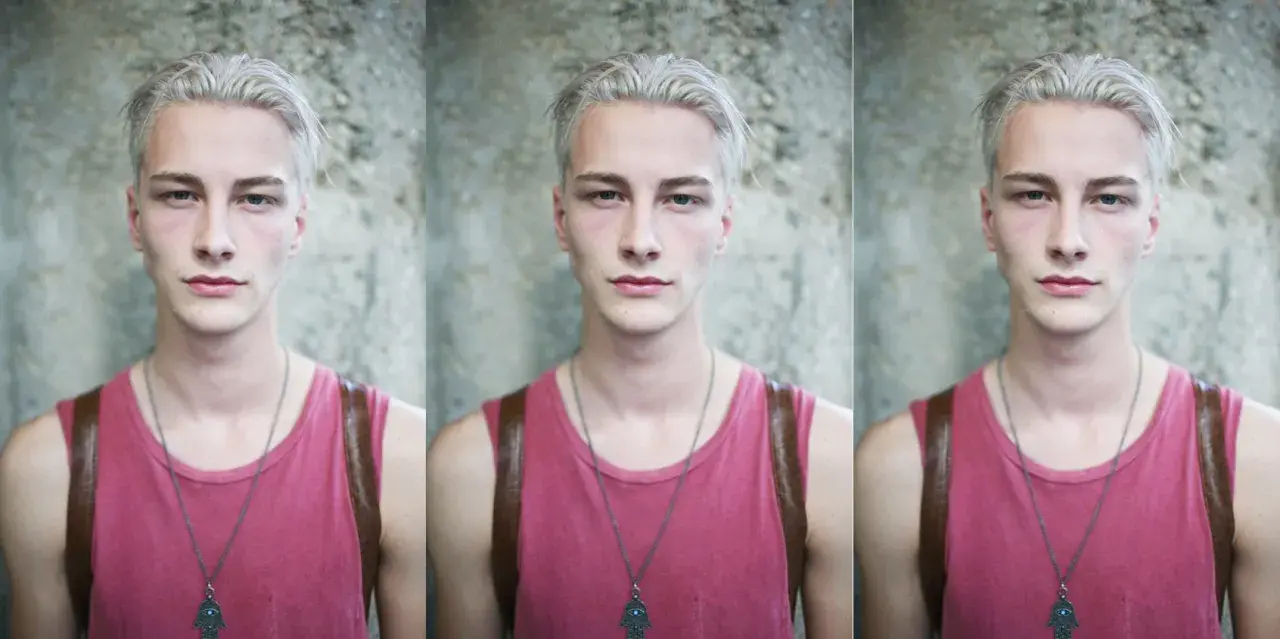 Joven con pelo blanco, viste camiseta rosa y un collar con un amuleto.