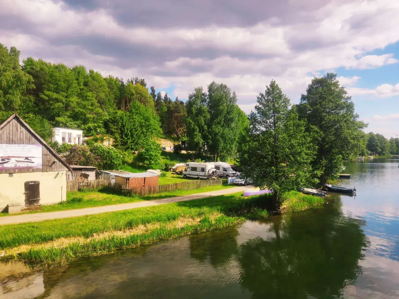 Malowniczy widok na jezioro i lasy, gdzie leżą Bory Tucholskie. Kemping z kamperami i łodziami przy brzegu.