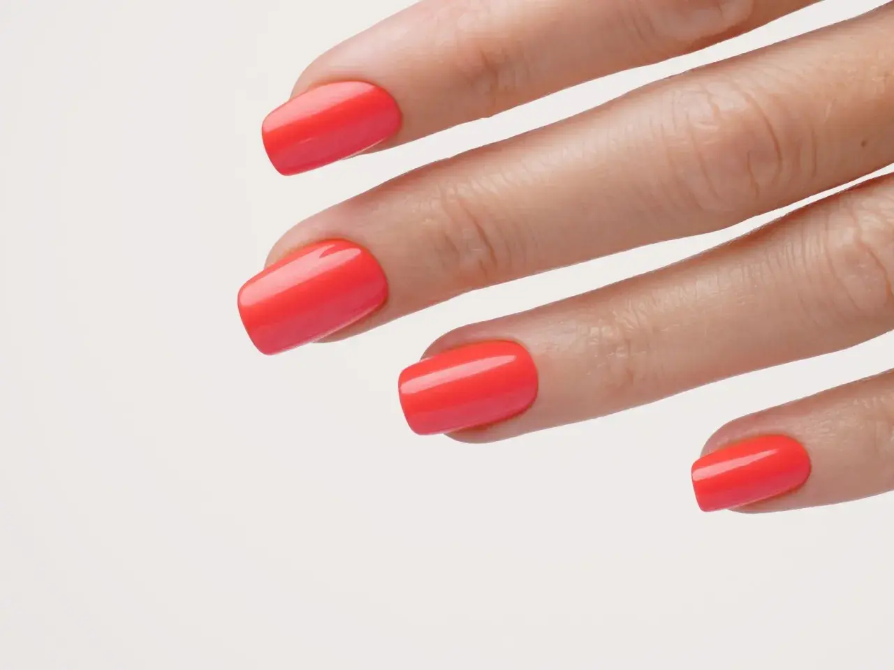 Main d'une femme avec un vernis corail vif, parfait pour un ongle vacances.