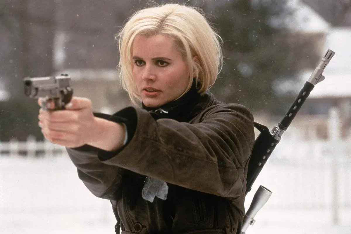 Geena Davis w filmach akcji, z pistoletem w dłoni i karabinem na ramieniu, gotowa do akcji w zimowej scenerii.