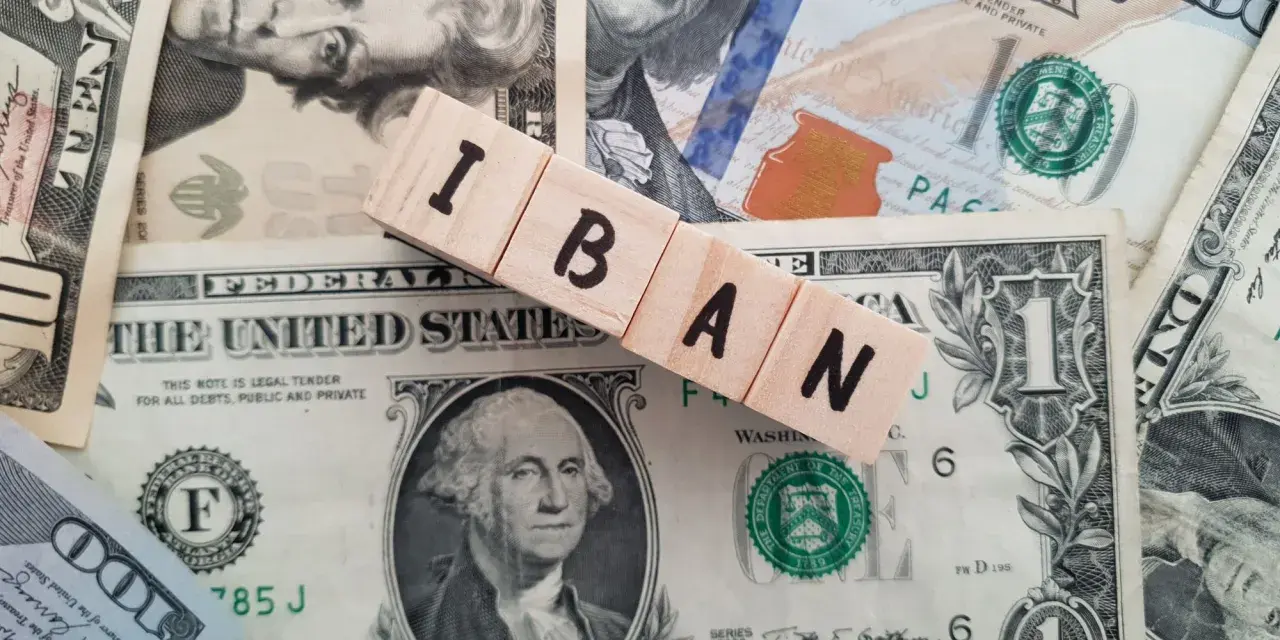 Drewniane klocki z napisem IBAN leżą na banknotach dolarowych. Dowiedz się, jak sprawdzić IBAN.