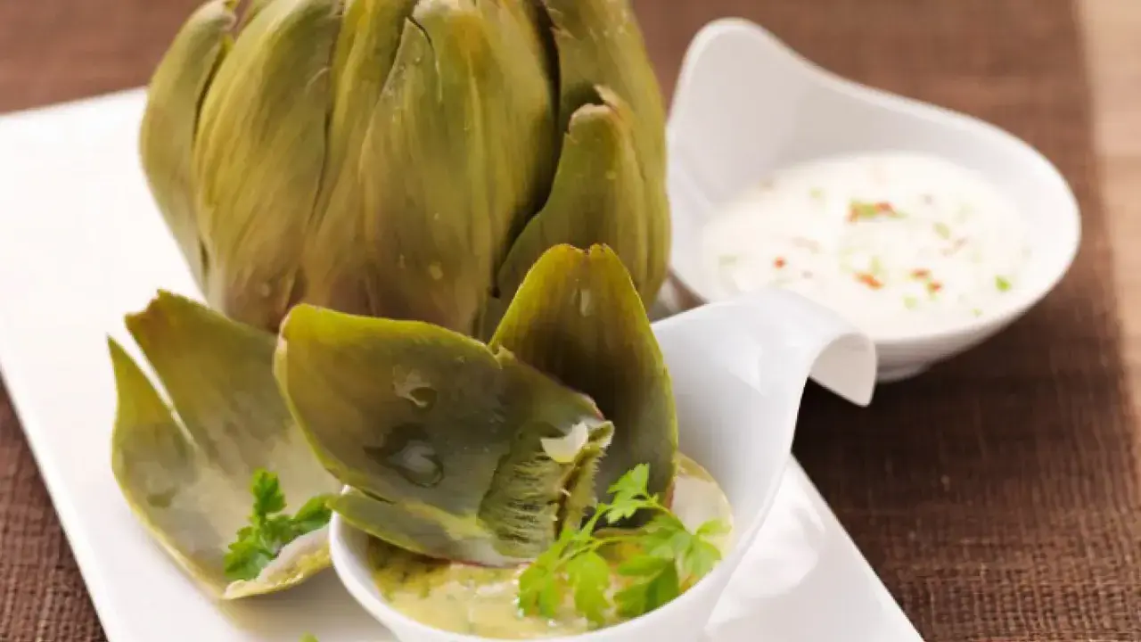 Alcachofas enteras cocidas, servidas con salsas para mojar. Una delicia para disfrutar.