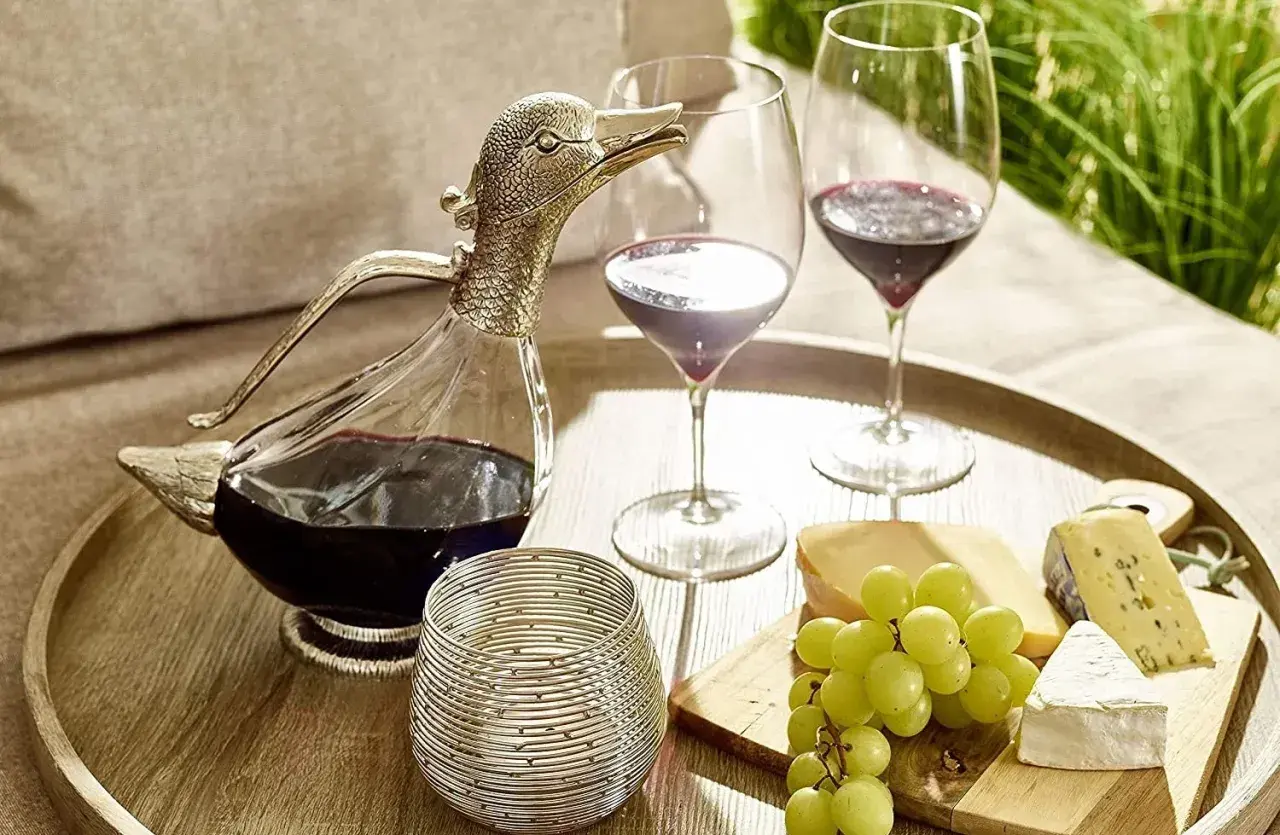 Dekantiert bedeutet, Wein in eine Karaffe zu füllen, um ihn zu belüften. Hier: ein Entenkaraffe mit Rotwein, Gläser, Käse und Trauben.