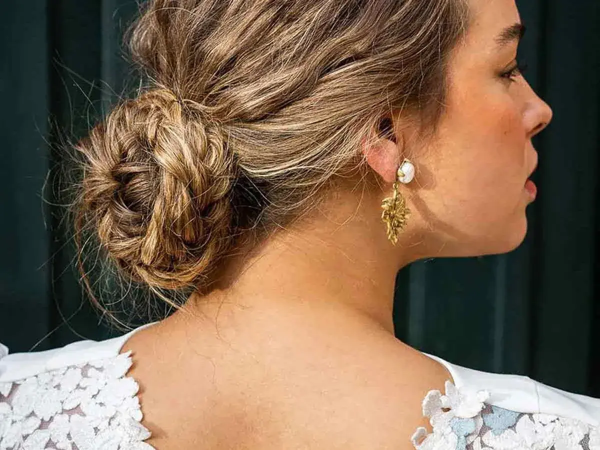 Elegante recogido pelo rizado boda invitada, con un moño trenzado y pendientes dorados.