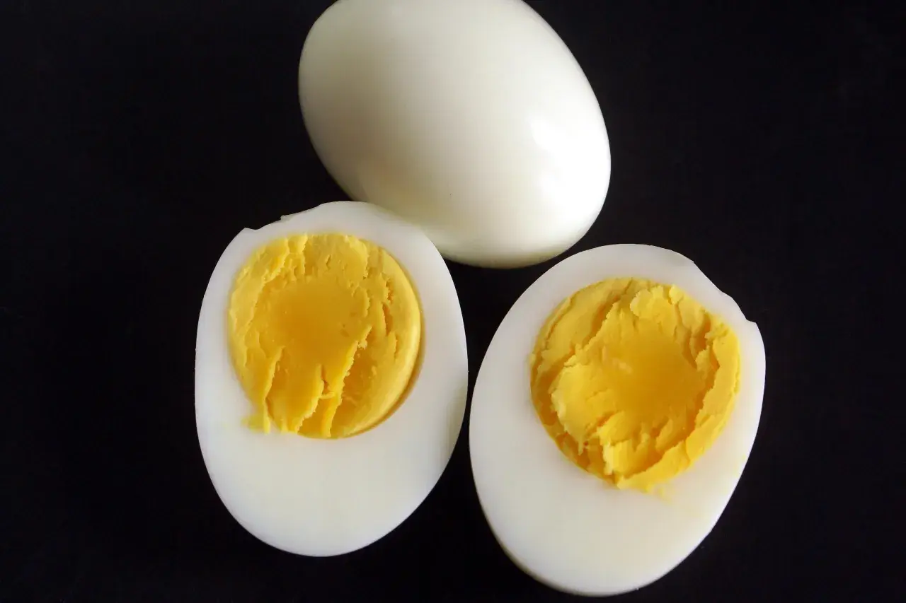 Un œuf entier et deux moitiés d'œufs durs sur fond noir, montrant le jaune bien cuit. Parfait pour une salade ou un en-cas.