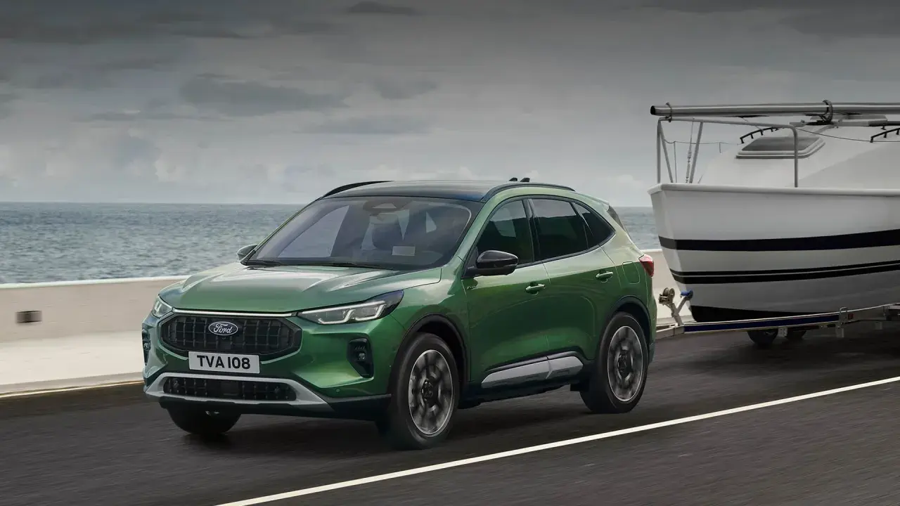 Zielony Ford Kuga z przyczepą i łodzią nad morzem. Sprawdź aktualną ford kuga cena.
